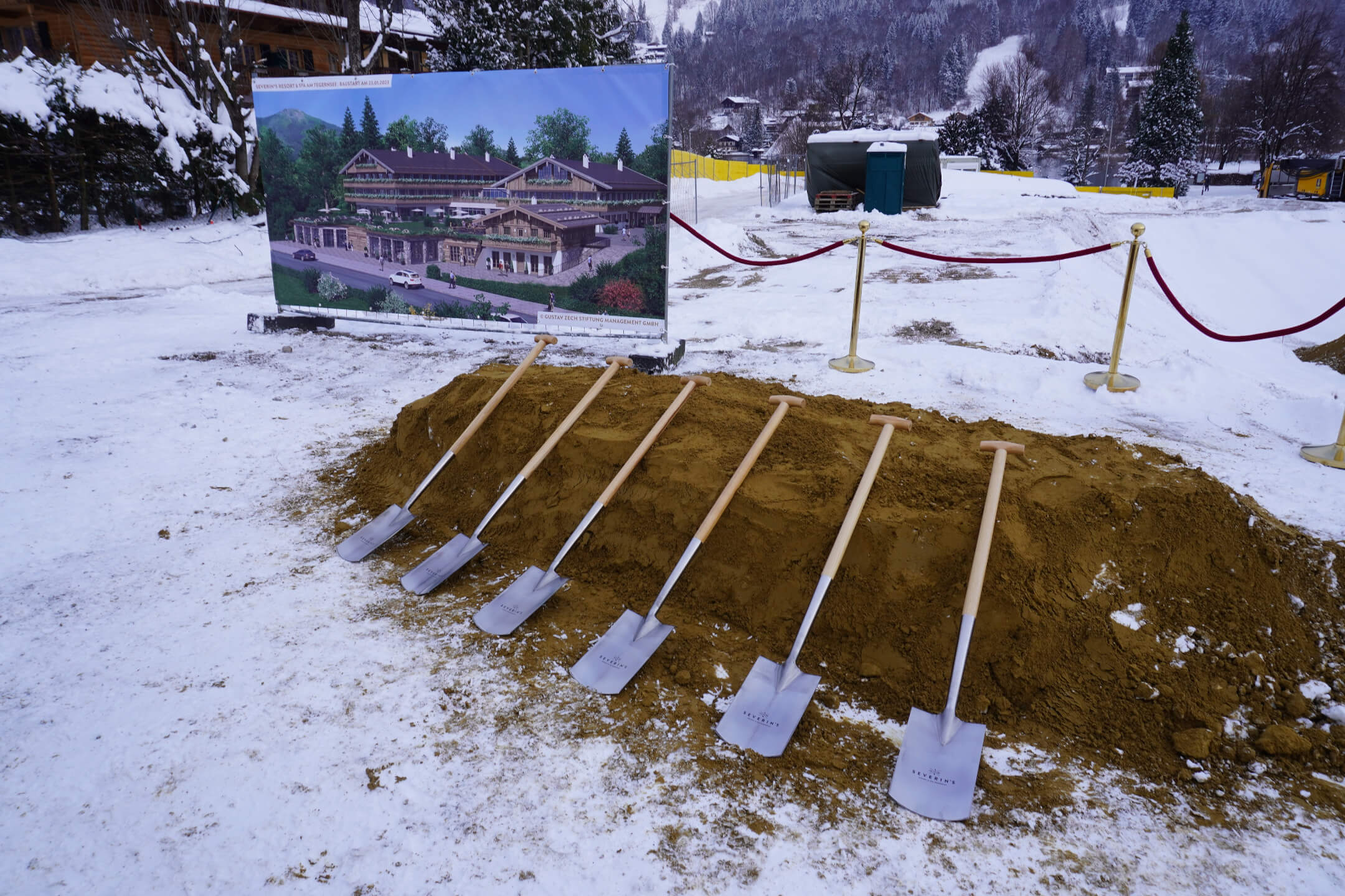 Bauvorhaben am Tegernsee: Sieben Spaten in Erde vor einem Plakat des geplanten Severin*s Resort & Spa im Schnee.