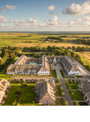 Luftaufnahme vom Severin*s Resort auf Sylt mit Innenhof, umgeben von grüner Landschaft und Meer im Hintergrund.
