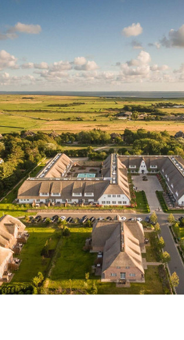 Luftaufnahme vom Severin*s Resort auf Sylt mit Innenhof, umgeben von grüner Landschaft und Meer im Hintergrund.