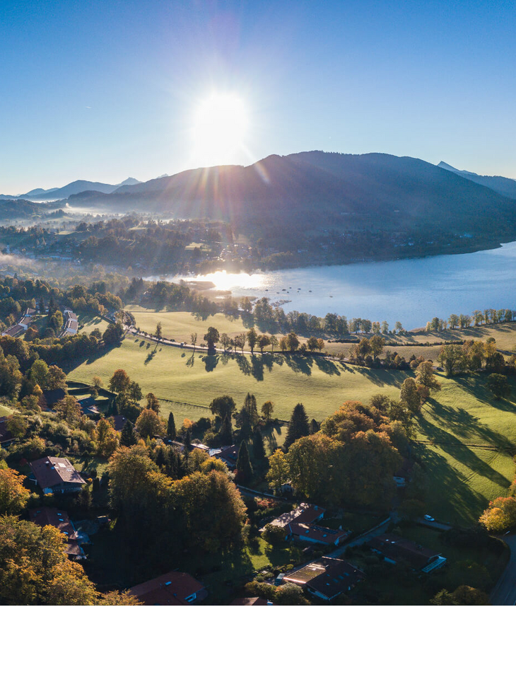 Blick auf den Tegernsee bei Sonnenaufgang, umgeben von grünen Wiesen und Bergen, nahe dem Severin*s Resort & Spa.
